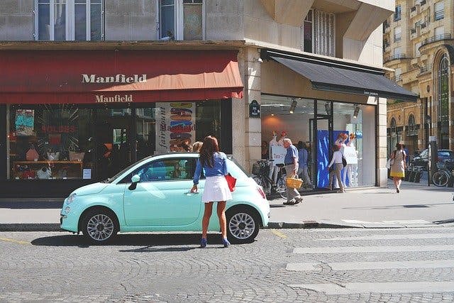 Frau steigt in italienischer Einkaufsmeile in einen mintgrünen Fiat ein