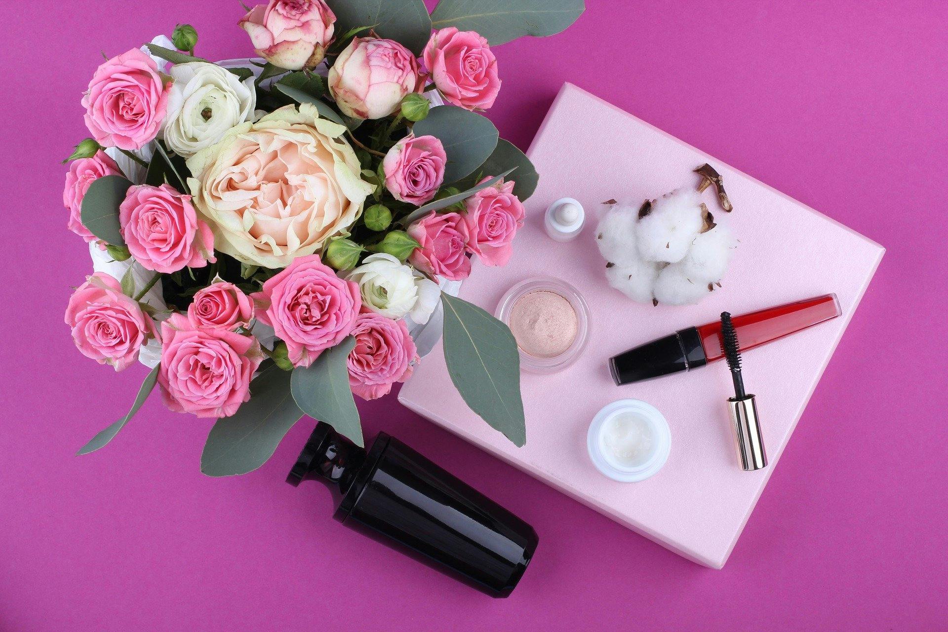 Kosmetik auf einem pinken Tisch mit Blumenstrauß.