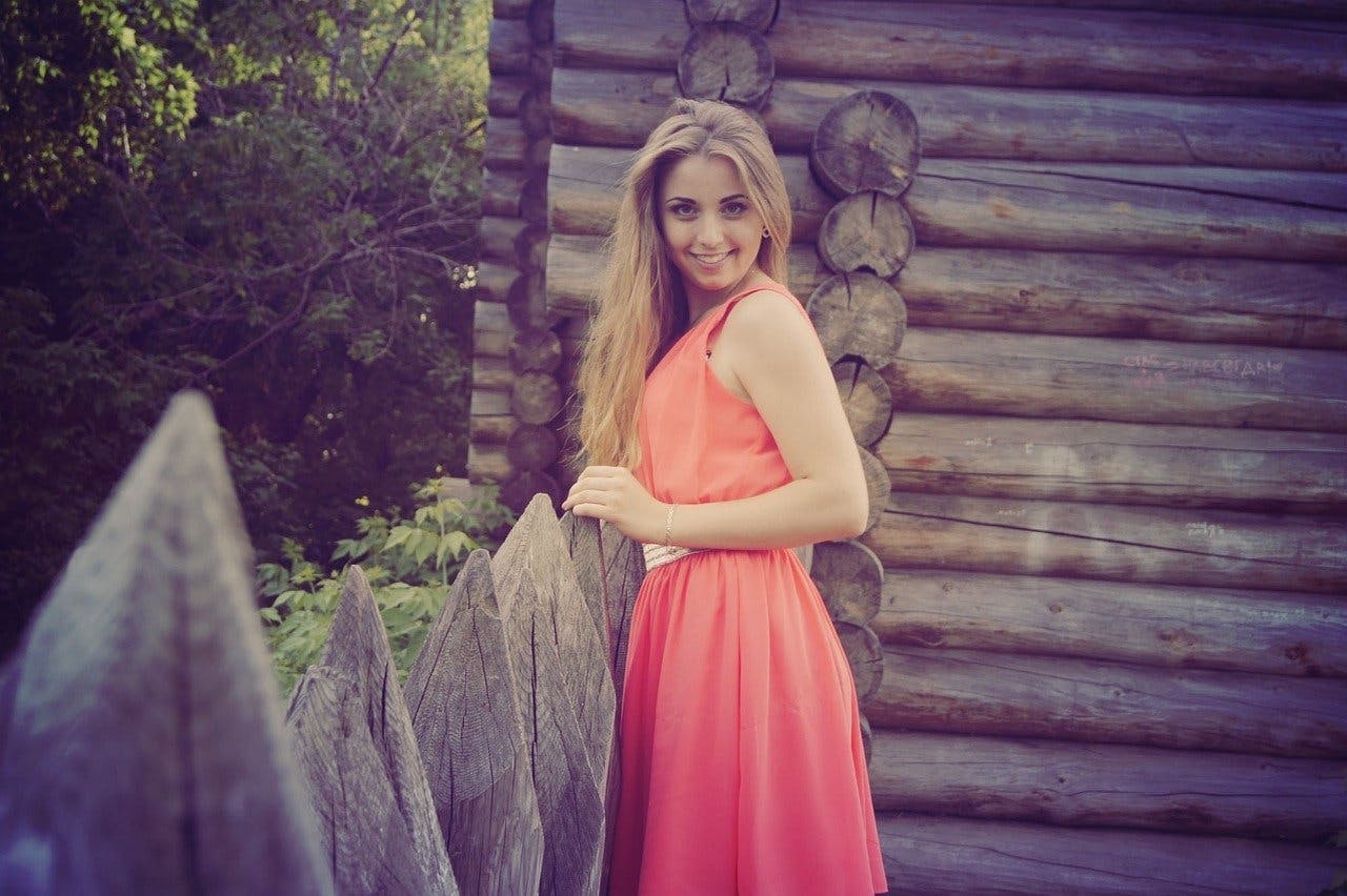 Frau in Sommerkleid steht an einem Holzzaun