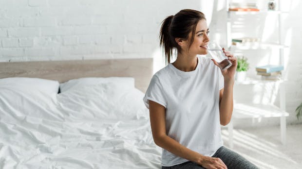 Eine Frau sitzt auf einem Bett und trinkt Wasser.