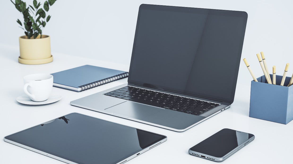 Ein Laptop, ein Tablet und ein Smartphone auf einem Schreibtisch.