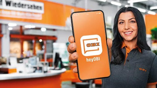 Eine OBI Mitarbeiterin hält ein Smartphone in die Kamera mit der geöffneten heyOBI App